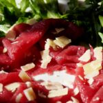 Bresaola su un tagliere di legno, con erbe aromatiche e spezie in primo piano.