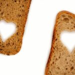 Una fetta di pane su un tavolo con un cuore e simboli di colesterolo e pressione sanguigna.