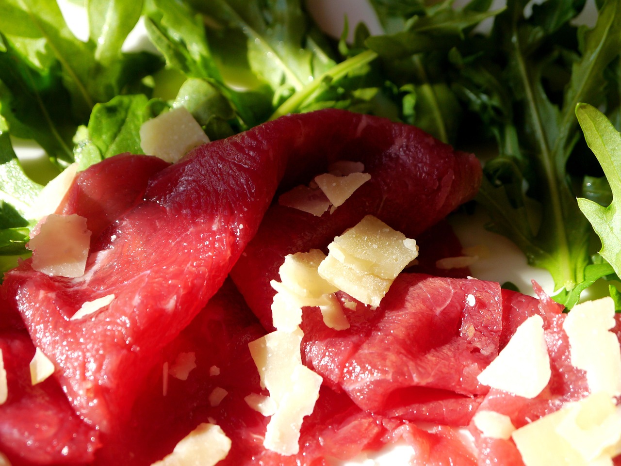 Bresaola appoggiata su un tagliere di legno, con fette sottili e decorazioni di rucola e pomodorini.