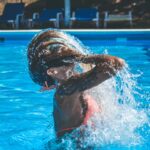 Donna con capelli bagnati che risciacqua i capelli dopo un bagno in piscina per prevenire doppie punte.